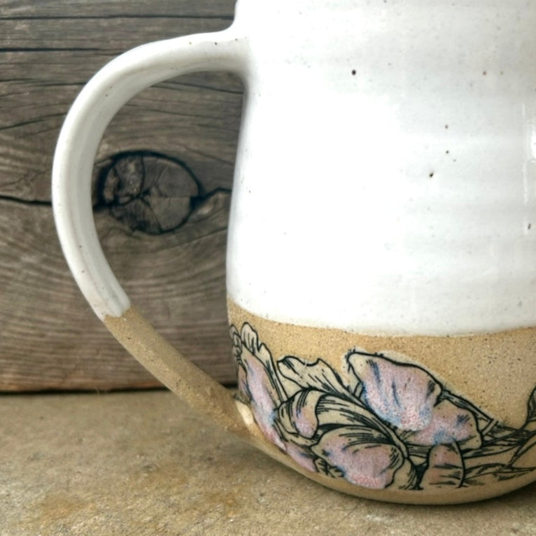 A ceramic mug with a floral pattern on the lower half, featuring a beige and white color scheme on a wooden background.