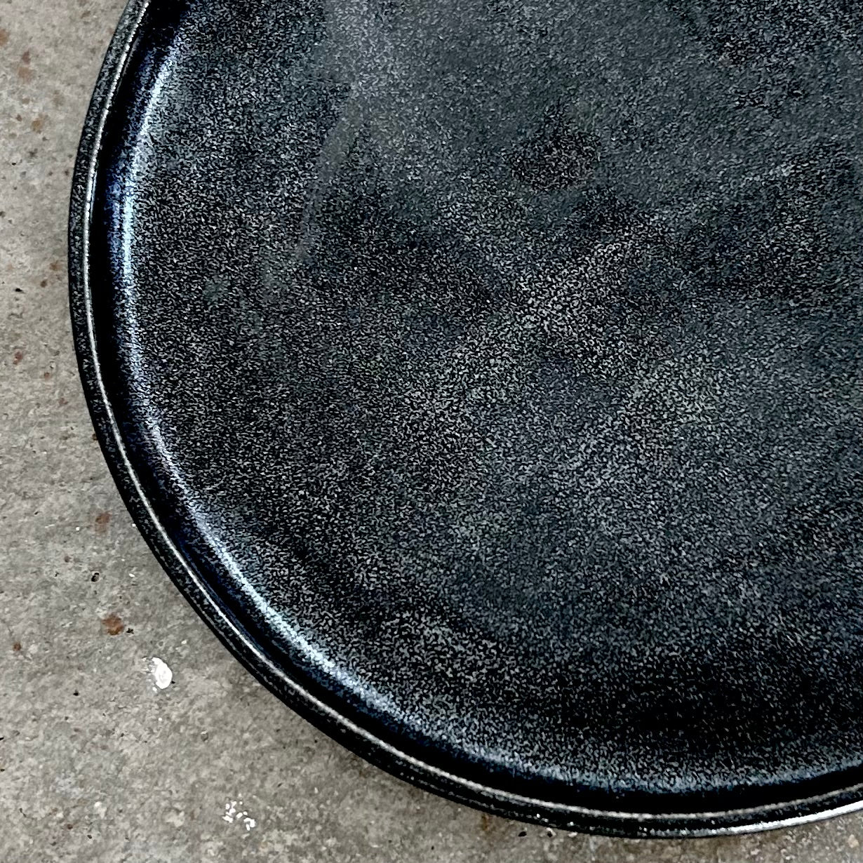 A close-up image of a hand-built, round, black pottery plate with a textured surface.
